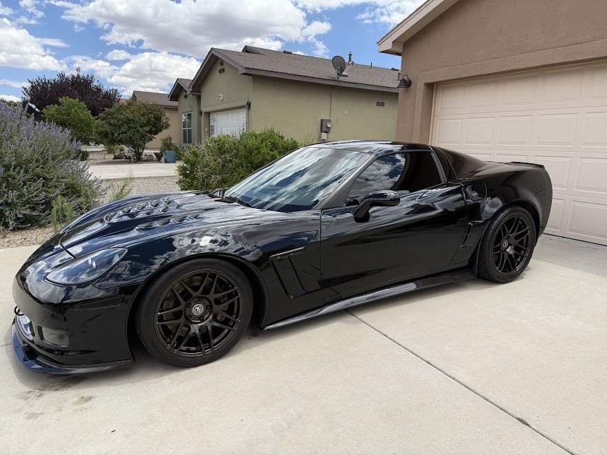 Black Corvette C6 with polished paint reflecting clouds across the body